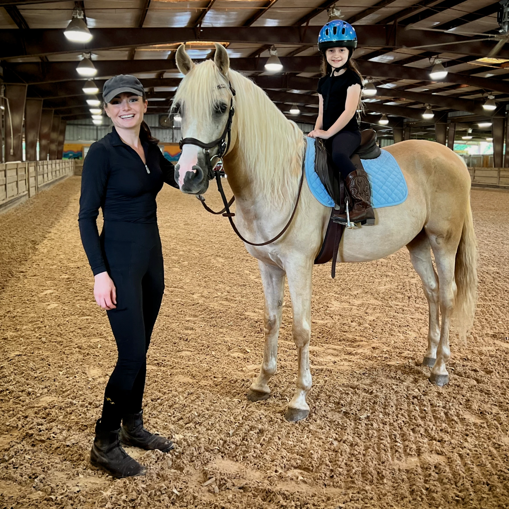 Instructor Madison Lareau standing beside a horse with a young rider in the saddle, inside an arena