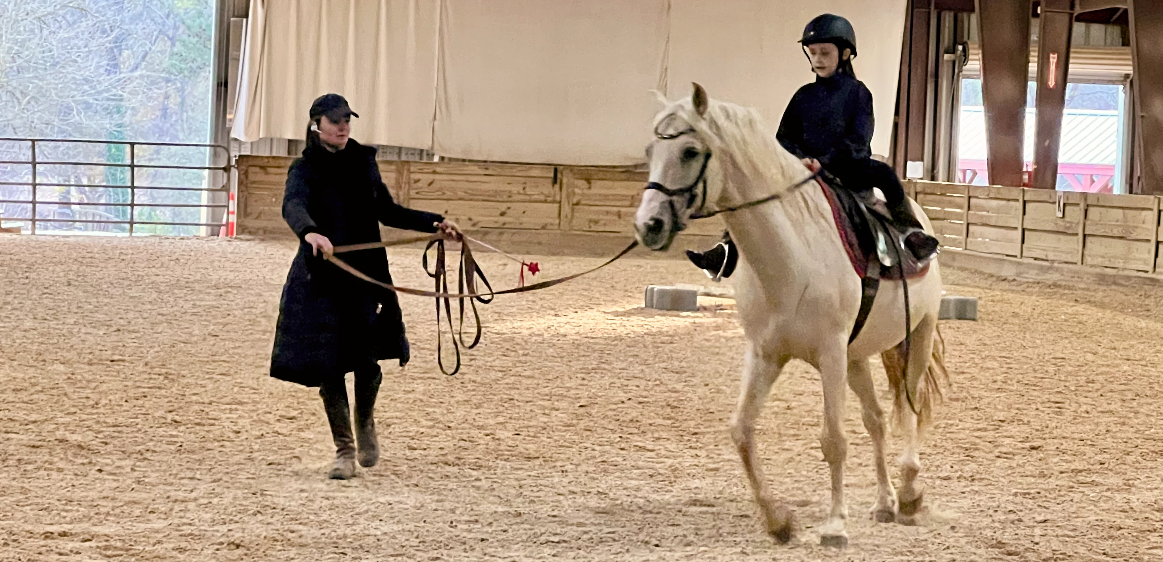 Instructor Madison Lareau standing beside a horse with a young rider in the saddle, inside an arena